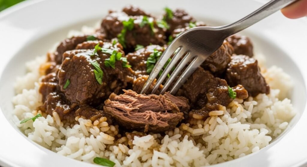 Prato branco com arroz e uma porção generosa de carne de panela que desmancha, com um garfo de prata mostrando a maciez extrema da carne.

