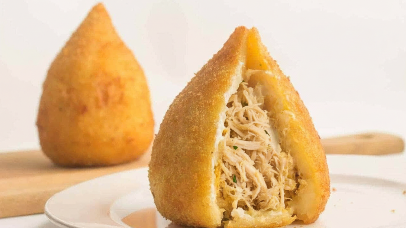 Coxinha de mandioca dourada e crocante cortada ao meio, mostrando o recheio cremoso de frango desfiado e a massa fina de mandioca.